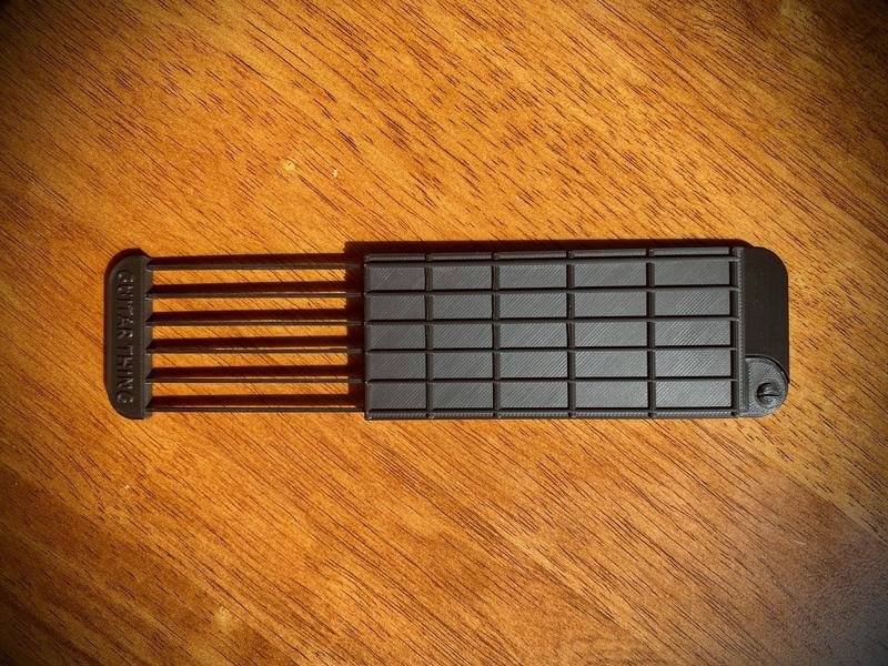 Guitar Thing slid open on a wooden table, its six pull-out strings extended