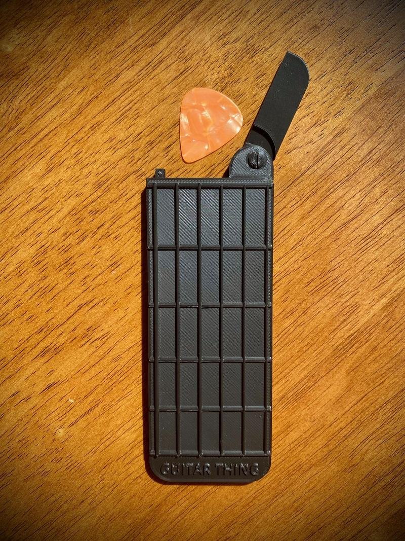 Guitar Thing with its pick compartment flipped open and a guitar pick tucked inside