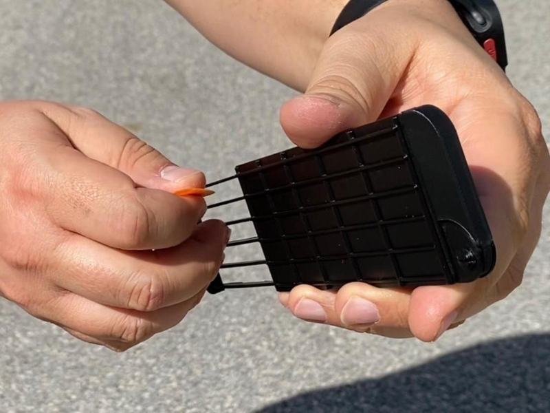 One hand holds Guitar Thing open while the other picks its pull-out strings with an orange pick